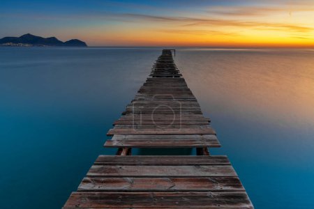 Peaceful sunrise seascape with an old wooden dock leading out into the calm ocean waters of Alcudia Bay