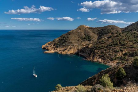 Photo for A sailboat moored in a bay of the Serra Gelada Natural Park with the Albir Lighthouse in the background - Royalty Free Image