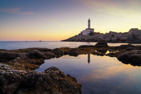 Peaceful landscape view of the Botafoc Lighthouse in Ibiza Town Port at sunsetwith reflections in tidal pools in the foreground
