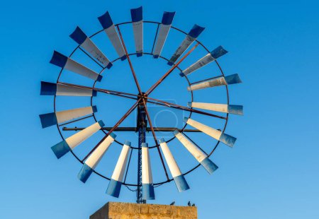 A close-up view of a modern windmill with steel blades in the interior of Mallorca under a blue sky