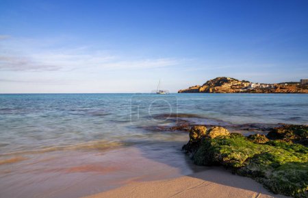 A view of the idyllic bay and beach of Cala Agulla in eastern Mallorca with a sailboat in the foreground