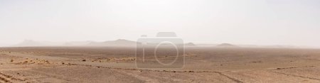 A panorama desert landscape with arid hlls in the distance under a hazy sandstorm sky in southern Morocco
