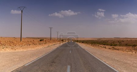 An endless desert highway and power lines leading through the rock and sand desert of southwestern Morocco