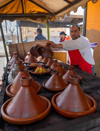 Foto de Timahdite, Marruecos - 6 de marzo de 2024: orgulloso cocinero marroquí mostrando sus comidas de tagine en su tienda de cocina en Timahdite - Imagen libre de derechos