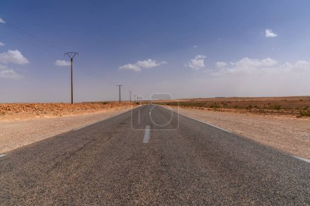 Téléchargez les photos : Une route désertique sans fin et des lignes électriques qui traversent le désert de roche et de sable du sud-ouest du Maroc - en image libre de droit