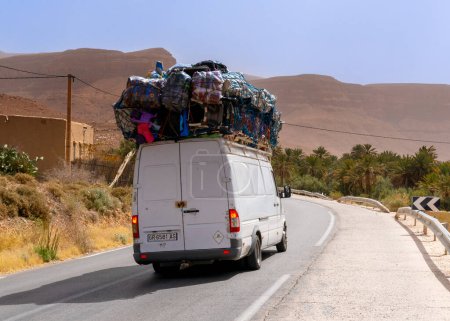 Foto de Achbaro, Marruecos - 7 de marzo de 2024: Autopista marroquí con una furgoneta transportadora gravemente sobrecargada que entrega mercancías a los pueblos del Alto Atlas - Imagen libre de derechos