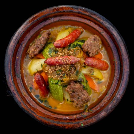 A top-down view of a Tagine Royal dish with vegetables and various meats and oriental spices on a black background