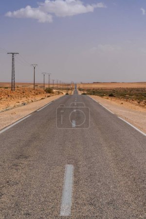Vue verticale d'une autoroute désertique sans fin et de lignes électriques menant à travers le désert de roche et de sable du sud-ouest du Maroc