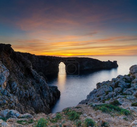 A view of the landmark stone arch of Pont d'en Gil on Menorca Island just after sunset