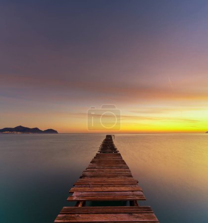 Peaceful sunrise seascape with an old wooden dock leading out into the calm ocean waters