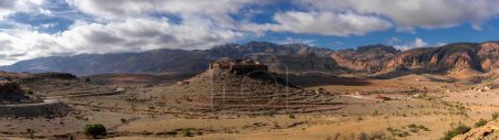 A panorama landscape view of the Altas mountains in Morocco with the Kasbah Tizourgane on the hilltop in the centre
