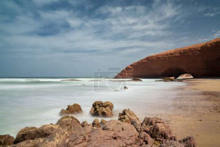 Una larga vista de la playa y el arco de roca en Legzira en la costa atlántica de Morroco