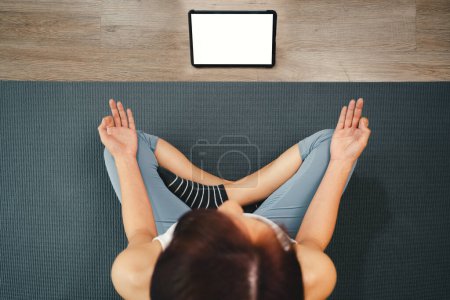 Photo for Yoga course at home with Technology tablet online, Top view of young woman sitting on yoga mat and using a tablet during meditation practicing yoga in sukhasana exercise at yoga studio - Royalty Free Image