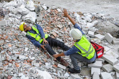 Photo for Accident in construction workplace, Knee accident from slip or stumble fall on the concrete scrap at construction site. Foreman helping injured colleague with first aid bag and wave hand to team help - Royalty Free Image