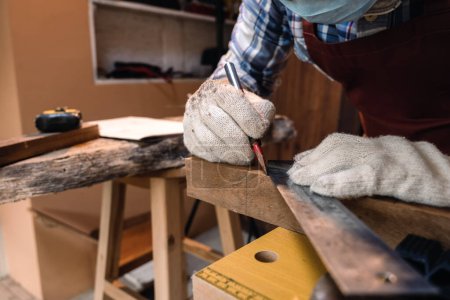 Foto de Cerrar la mano del carpintero utilizando la herramienta de regla de ángulo cuadrado y el lápiz para marcar la posición en la madera para cortar en el taller de carpintería. - Imagen libre de derechos