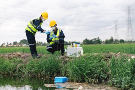 Photo for Two Environmental Engineers Inspect Water Quality and Take Water Samples Notes in The Field Near Farmland, Natural Water Sources maybe Contaminated by Toxic Waste or Suspicious Pollution Sites. - Royalty Free Image