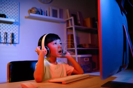 Asian Kid Boy intenta Gaming Stream en el escritorio de la computadora para la diversión y el entretenimiento en el hogar, explorando el viaje virtual del juego del mundo. Desarrollar habilidades a través del juego, la transmisión y el vlogging para niños