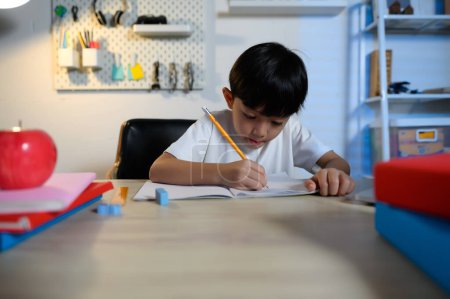 Téléchargez les photos : Asian Kid Boy se concentre sur les devoirs et l'apprentissage seul dans la chambre à la maison, Serious Asian Kid se concentre sur les devoirs, les études et le succès, les devoirs et l'éducation des enfants asiatiques Concept. - en image libre de droit