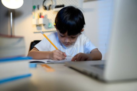 Téléchargez les photos : Asian Kid Boy se concentre sur les devoirs et l'apprentissage seul dans la chambre à la maison, Serious Asian Kid se concentre sur les devoirs, les études et le succès, les devoirs et l'éducation des enfants asiatiques Concept. - en image libre de droit