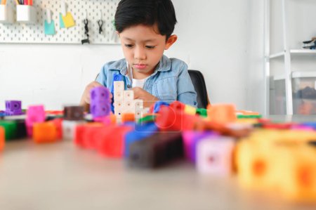 Foto de Niño pequeño asiático jugando cubos de plástico coloridos en el escritorio en casa. Aprendizaje y educación sobre contar cubos en matemáticas, desarrollar el cerebro y la meditación mientras se juega. - Imagen libre de derechos