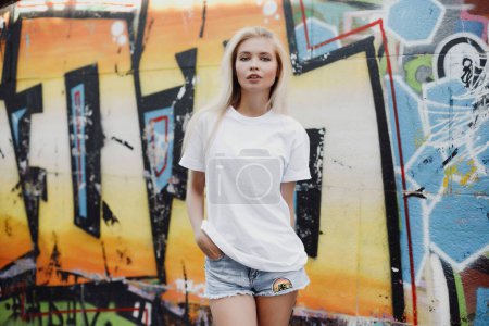 Téléchargez les photos : Fille blonde en t-shirt blanc et short près du mur de graffiti - en image libre de droit