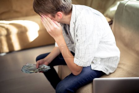 Photo for Boy is holding on to his head. A sad teenager with a wad of dollars in hands thinks about a future career. - Royalty Free Image
