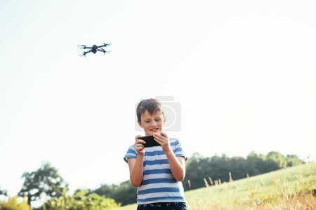 Téléchargez les photos : Enfant regarde la vidéo sur le smartphone depuis la caméra du drone. quadcopter drone gris foncé avec appareil photo numérique et capteurs volants - en image libre de droit