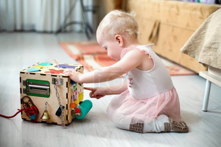 Photo for Activity Board. The baby learns the numbers on the clock on the bisiboard. Early development of children with a playful wooden cube toy Montessori. - Royalty Free Image