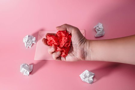Foto de Hand of aggressive and frustrated man squeezing heart out of crumpled paper. envelope with lumps of paper scattered. Letter to a Loved One on Valentine's Day - Imagen libre de derechos