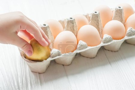 Photo for The child takes out a golden egg from the egg tray. A dozen chicken eggs on the table. Rise in price of products in Ukraine. New egg prices - Royalty Free Image