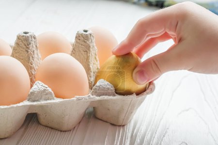 Téléchargez les photos : The child takes out a golden egg from the egg tray. A dozen chicken eggs on the table. Rise in price of products in Ukraine. New egg prices Concept of success. Easter egg hunt. - en image libre de droit