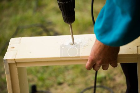 Photo for Beekeeper in protective suit collects hives from plastic blanks. Collect hive case to install frames. man holds drill with screwdriver and works outdoor. - Royalty Free Image