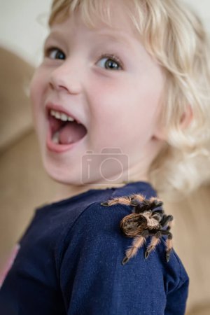 Photo for The child was frightened by a huge spider crawling on his back. The baby is terrified of the tarantula jumping on her shoulder. - Royalty Free Image
