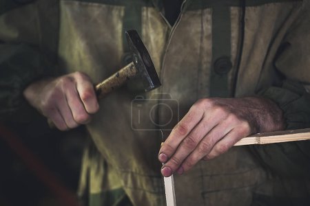 Photo for Man clogs a nail wooden frame for bees. Men's hands with long thin fingers hold wooden frame. - Royalty Free Image