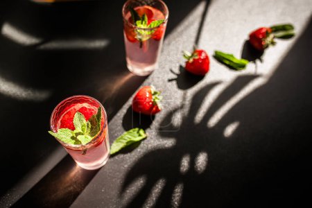 Téléchargez les photos : Cocktail de fraises fraîches. Un verre de soda d'été à la fraise boit sur fond sombre avec des ombres tendance. cocktail punch boisson d'été de baies rouges - en image libre de droit