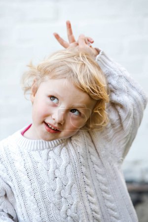 Téléchargez les photos : Portrait de drôle petite fille blonde levant les yeux et montrant la victoire des doigts" - en image libre de droit