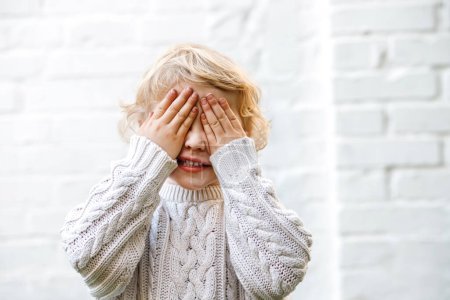 Téléchargez les photos : Une fille de quatre ans couvre ses yeux avec ses mains dans un g ludique mignon - en image libre de droit
