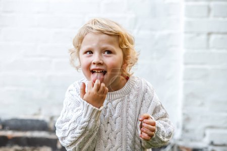 Photo for A little girl indulges and shows her tongue. Little girl sticking her fingers in her mouth - Royalty Free Image
