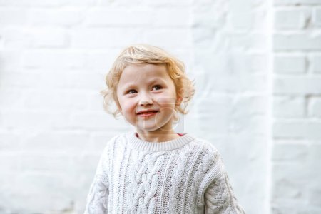 Photo for Happy little girl in white sweater smiling sweetly. heartwarming smile that could brighten anyones day - Royalty Free Image
