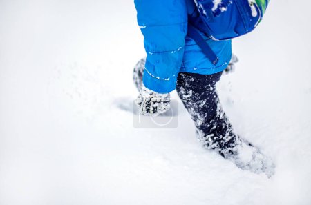 Foto de Piernas de un niño caminando en la nieve. Actividades de invierno Un joven estudiante regresa de la escuela con una mochila después de una nevada en invierno. - Imagen libre de derechos