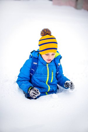 Foto de Lindo niño divirtiéndose con nieve en el parque de invierno. Niño feliz jugando con la nieve en el parque de invierno. - Imagen libre de derechos