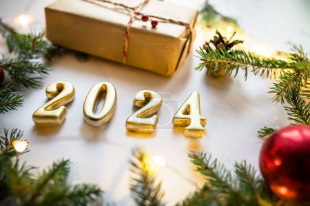 Photo for Golden numerals 2024 on white background with craft gift, christmas tree branches and red decorations and christmas lights. - Royalty Free Image
