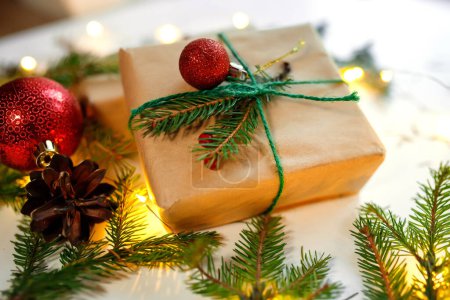 Téléchargez les photos : Cadeau de Noël enveloppé dans du papier kraft et décoré de boules rouges et de branches de sapin sur fond blanc. - en image libre de droit