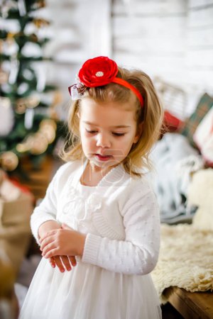 Photo for Little girl in a white dress on the background of a Christmas tree. - Royalty Free Image