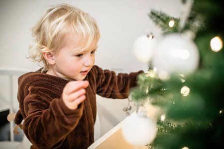Photo for Cute little girl standing near christmas tree and pointing with finger - Royalty Free Image