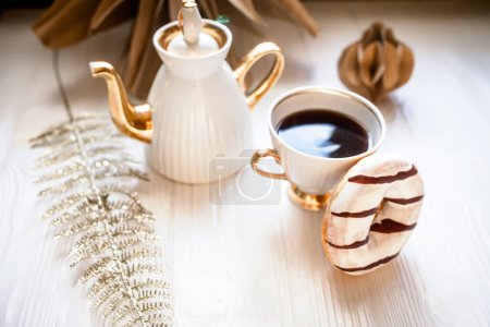 Foto de Una taza de café y rosquillas de chocolate sobre un fondo de madera blanca. Decoraciones de Navidad de papel Kraft hecho a mano. - Imagen libre de derechos