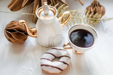 Téléchargez les photos : Tasse de café avec beignet au chocolat blanc et chocolat d cor sur fond de bois blanc. Décorations de Noël en papier kraft fait main - en image libre de droit