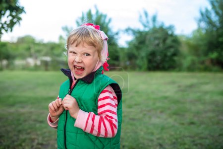 Foto de Niña divertida gritando con la boca abierta sobre el fondo de un prado con hierba. - Imagen libre de derechos