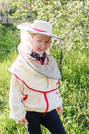 Téléchargez les photos : Petite fille en costume d'apiculteur au printemps parmi les fleurs de cerisier - en image libre de droit