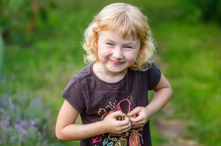 Foto de Niña entrecerrando los ojos mientras juega en el parque en verano. Retrato de una linda niña rubia en el jardín de verano. - Imagen libre de derechos